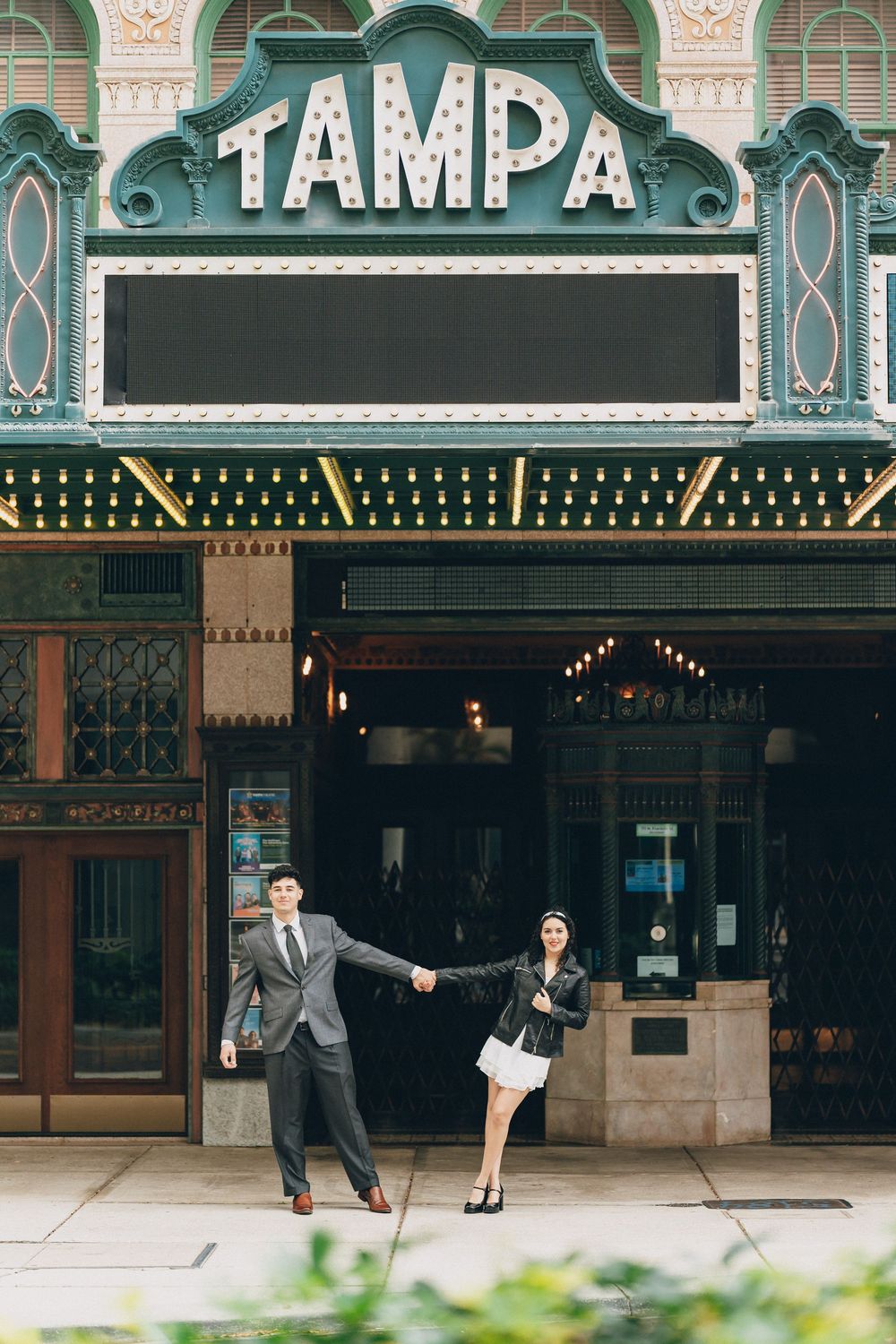 A couple poses playfully in front of the historic Tampa Theatre's iconic marquee and facade.