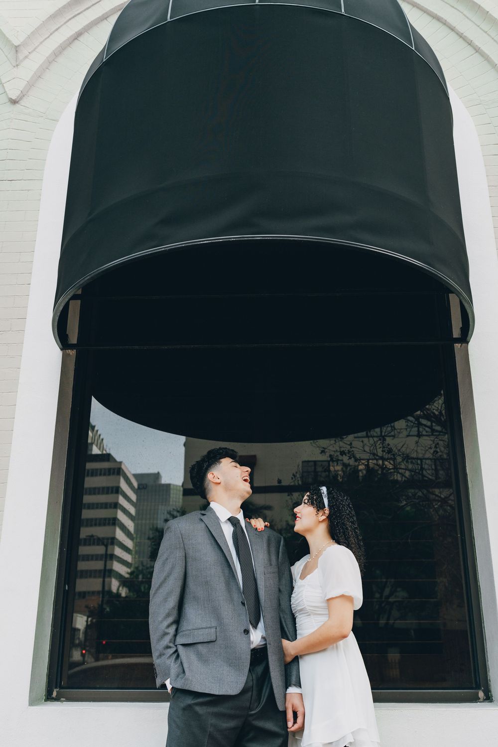 A couple shares a romantic moment under a black awning against a white building.