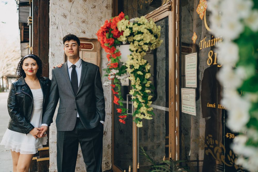 A couple poses together near a doorway decorated with colorful floral arrangements.