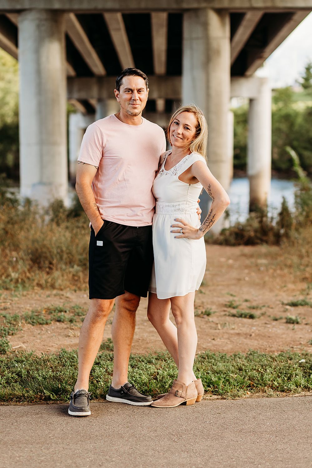 Couple in casual summer outfits standing together in series of romantic poses under a bridge or overpass.