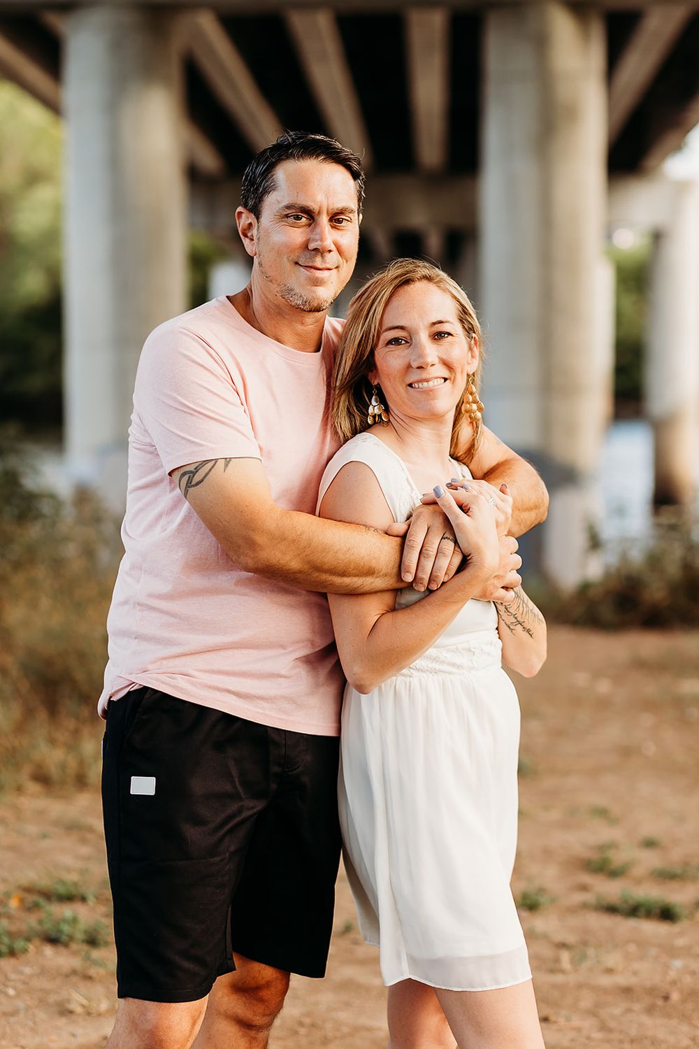 A couple shares playful and candid moments together while posing outdoors under a row of tall pillars.