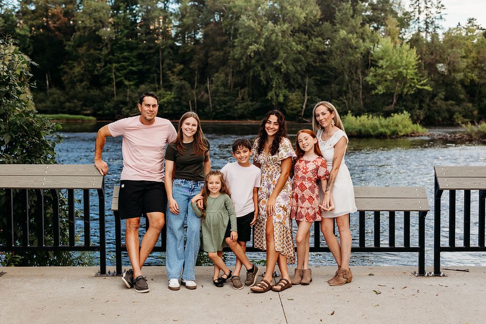 Multi-generational group in casual summer attire poses together on a wooden dock near a serene lake during sunset.