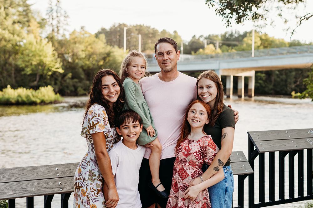 A group poses together outdoors on a wooden deck near a lake during golden hour.