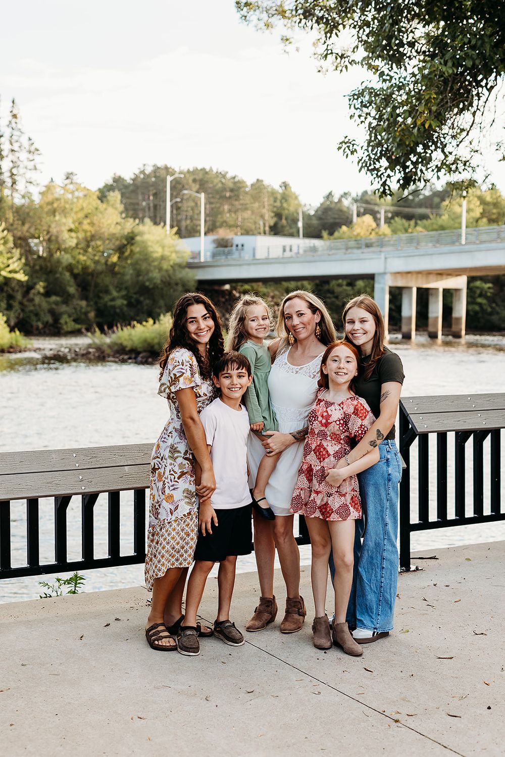 Group of friends standing together on a wooden pier during sunset in casual summer outfits.