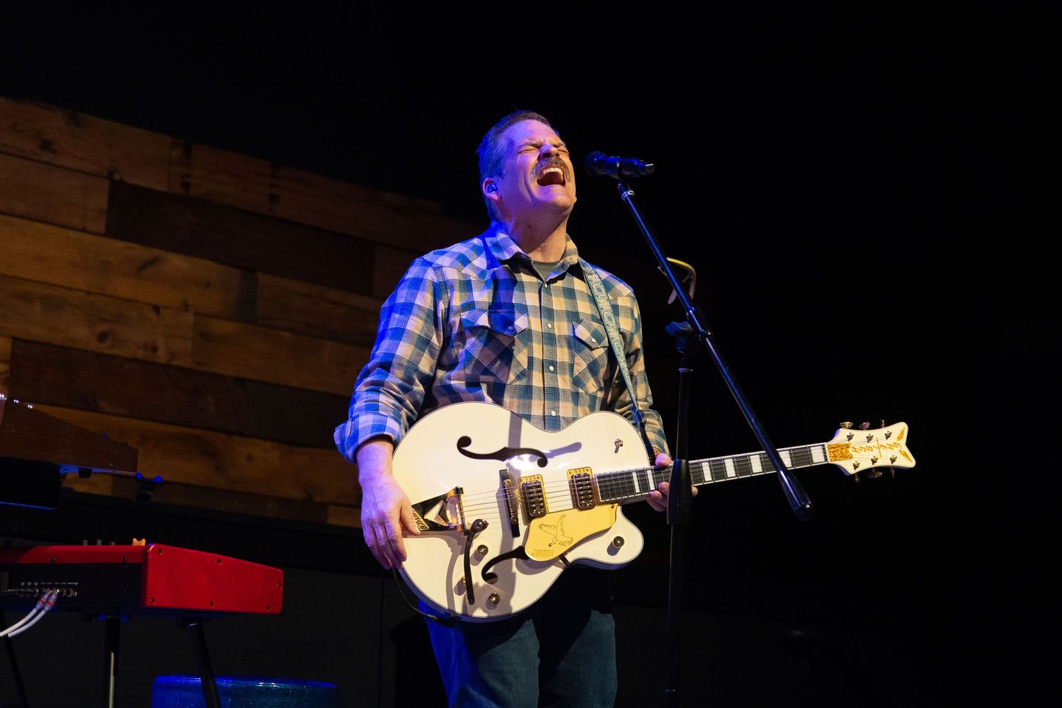 Musician performs on stage with a banjo under blue stage lighting during a live concert performance.