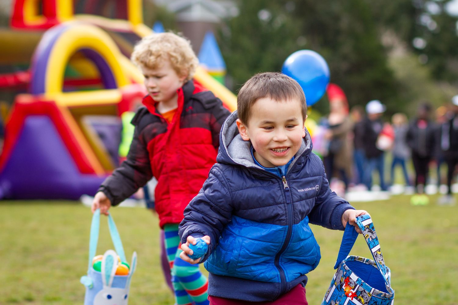 A blurry bouncy house and play area at an outdoor event with children playing in front of colorful inflatables.