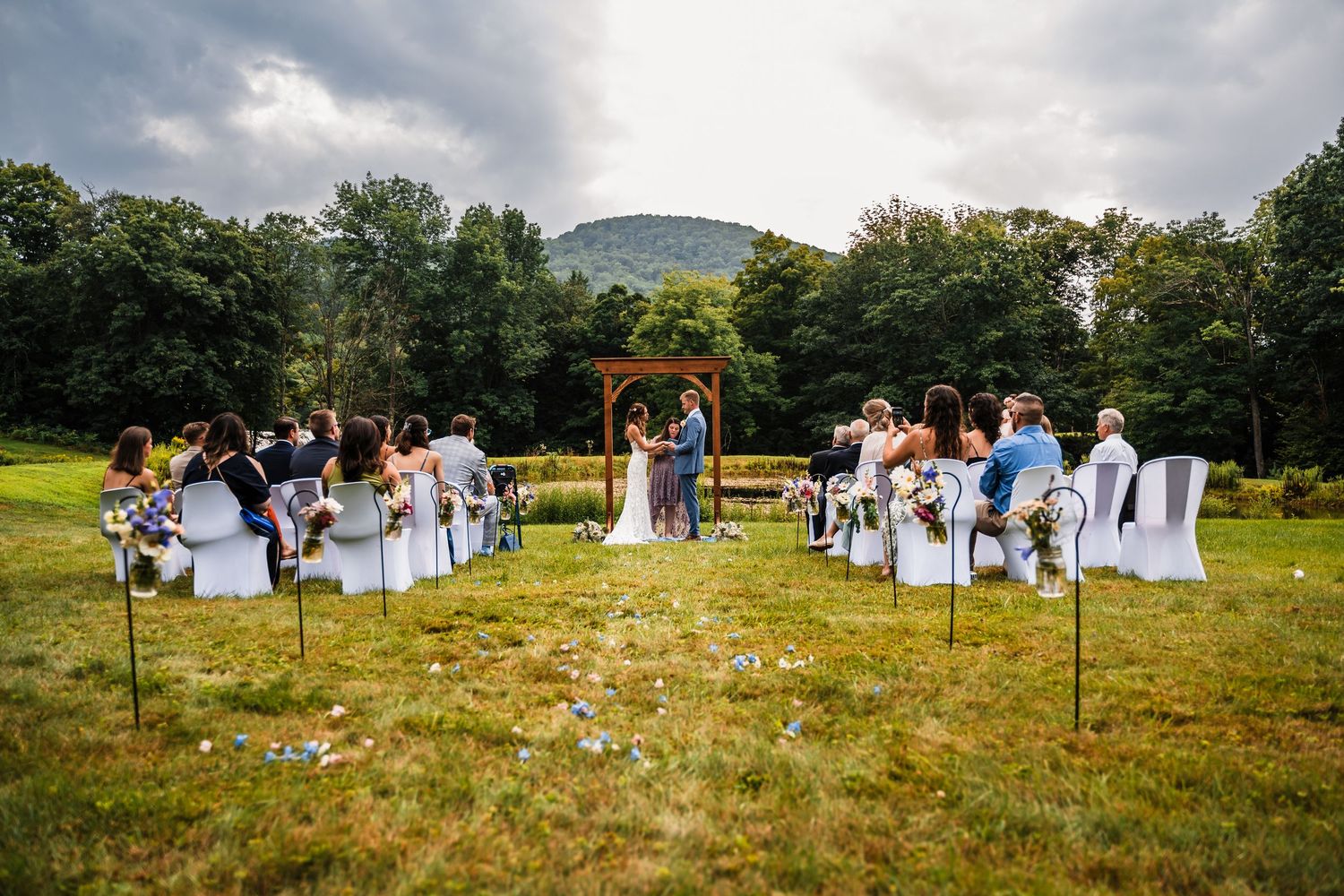 Outdoor wedding ceremony setup in a grassy field with mountain backdrop and white chairs for guests.