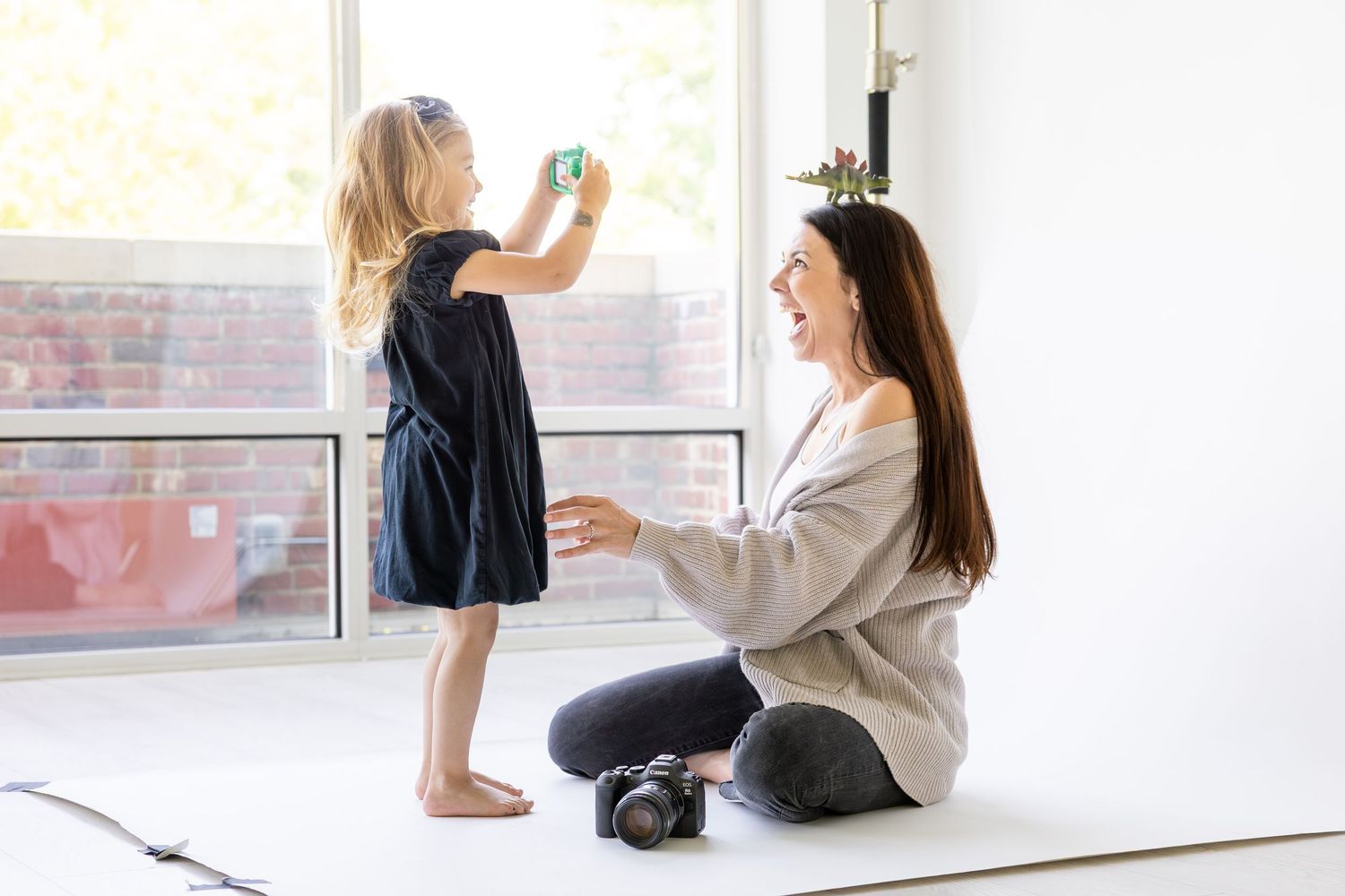 Parent and child taking photos together near a bright window in a minimalist white room at Studio 577.