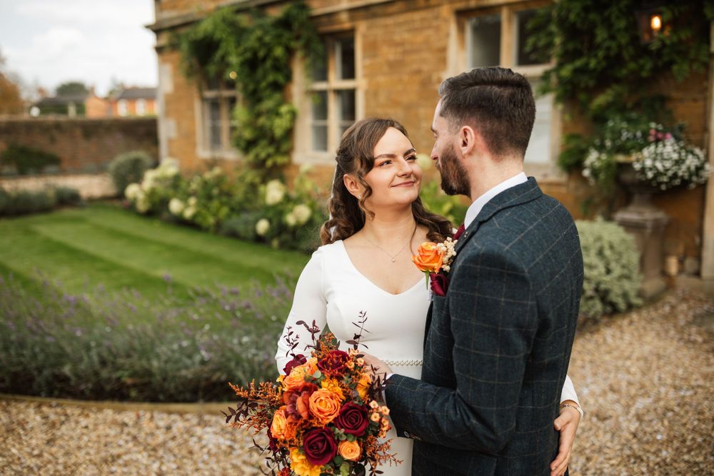 A romantic wedding couple share an intimate moment in a garden setting with a vibrant autumn bouquet.