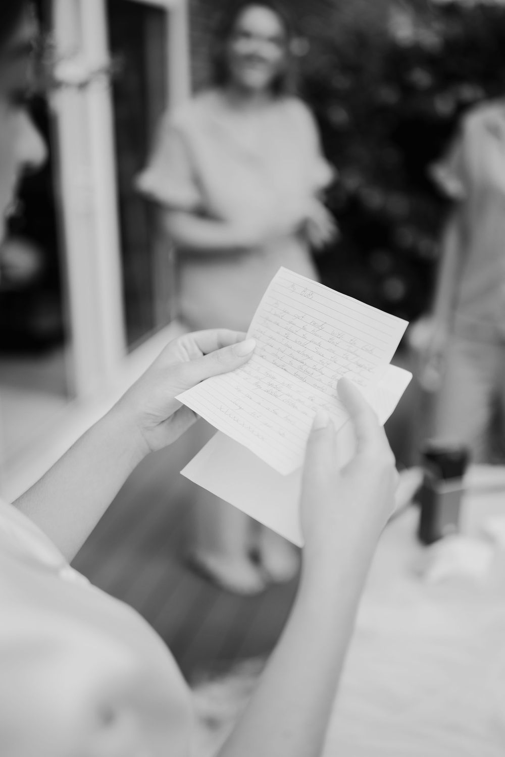 Bride reads handwritten letter in black and white photo during wedding preparations outdoors.