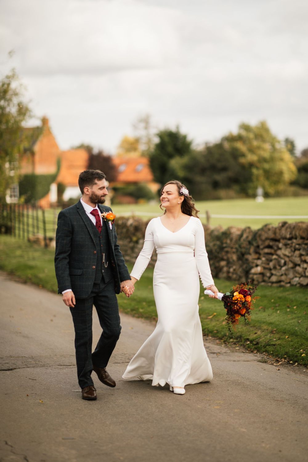 A joyful couple walking along a country path during an autumn wedding celebration.