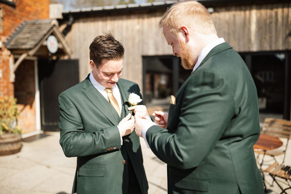 Two men in formal suits adjust boutonnieres before the ceremony.