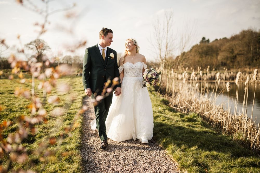 A couple walks along a lakeside path surrounded by winter reeds and natural landscape.
