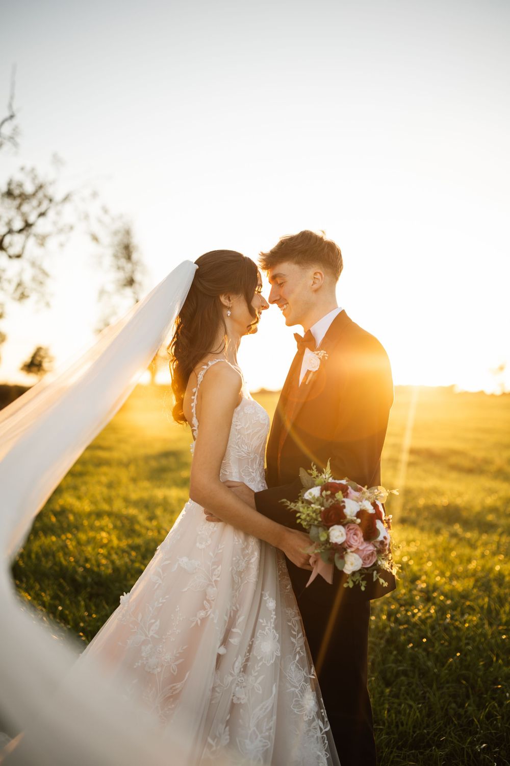 Romantic sunset wedding photo in a field of wildflowers with golden light streaming through.