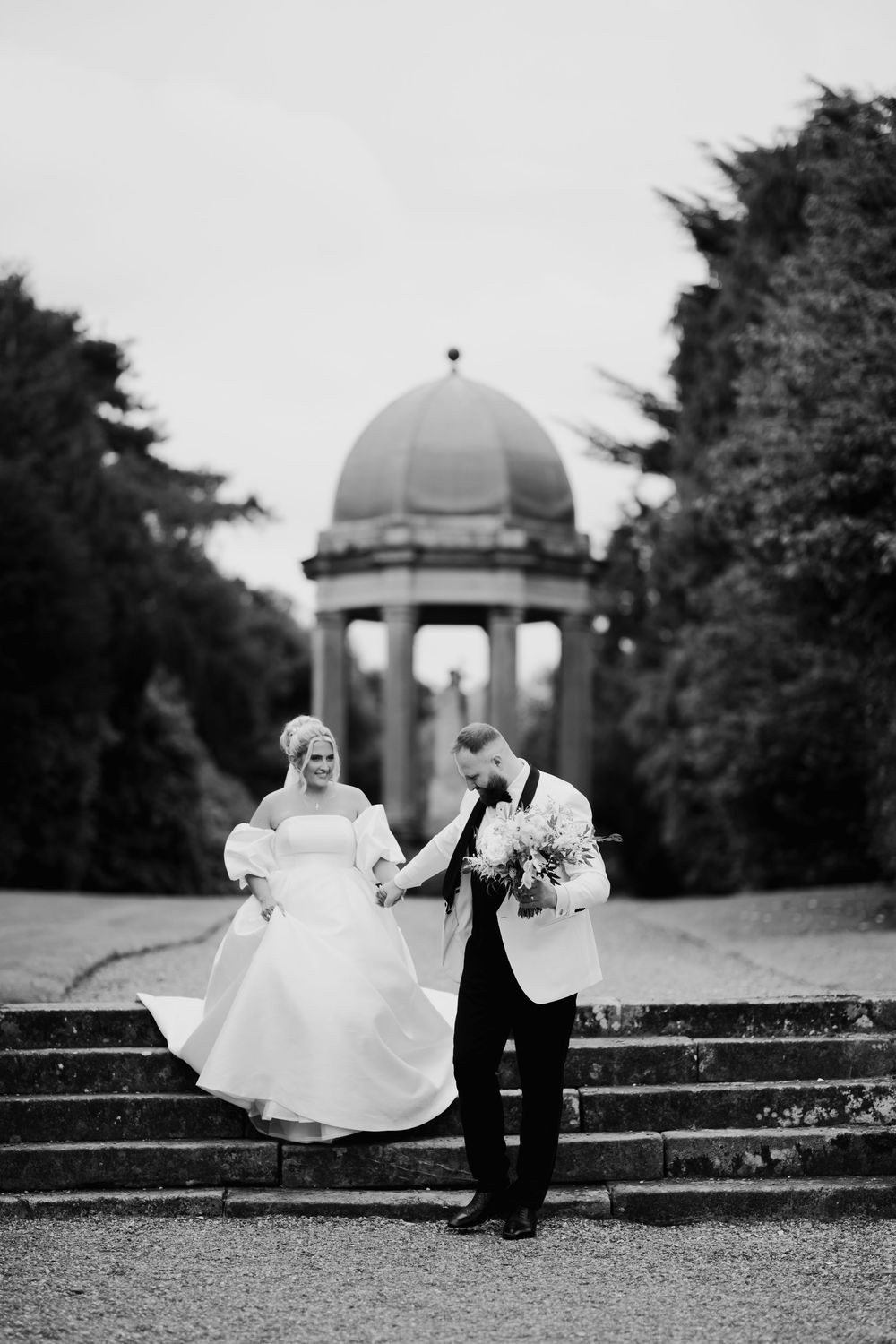 Black and white photo of a couple on garden steps with domed structures in background at an elegant venue.