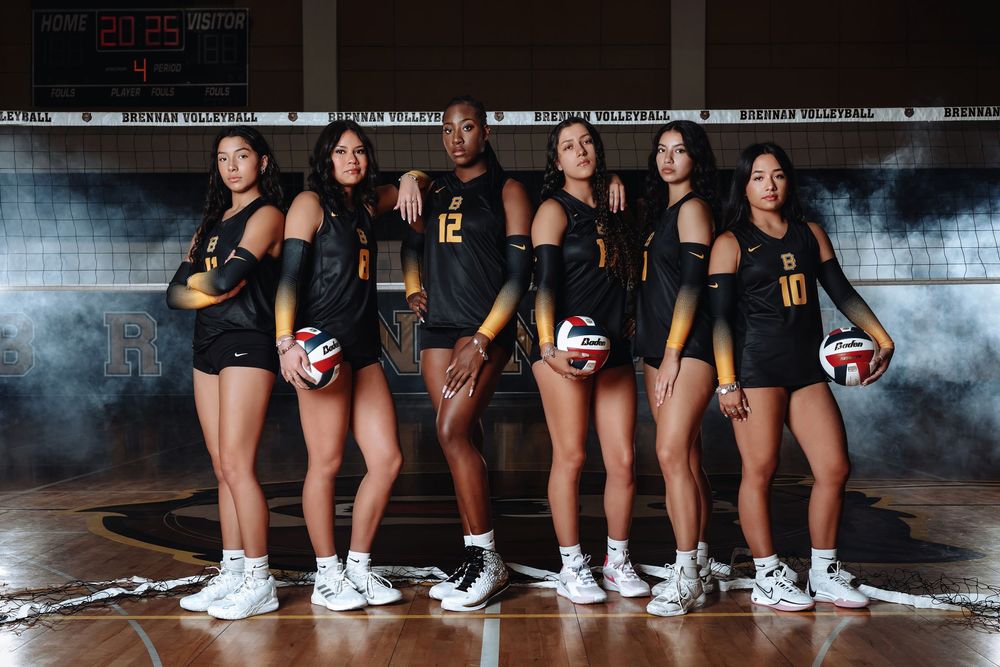 A volleyball team poses in black uniforms on a dark court with dramatic lighting and smoke effects.