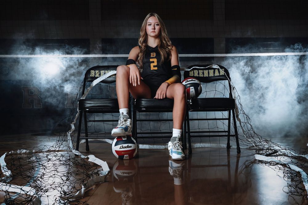 High school volleyball player sits on bench in dramatic lighting with fog effect for sports portrait photoshoot.