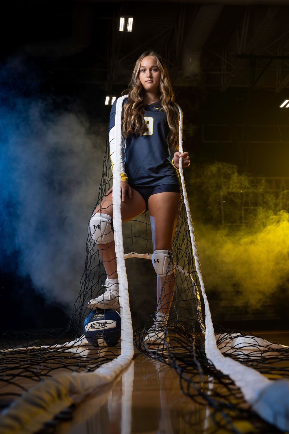 Volleyball player poses in a dramatic setting with smoke effects and dramatic lighting on the court.