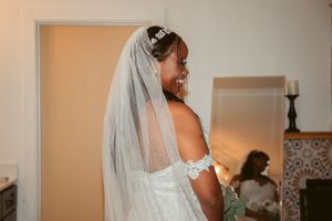 Bride in white lace dress and flowing veil getting ready in softly lit room.