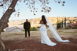A romantic wedding portrait showing newlyweds against a scenic hilltop backdrop at sunset.