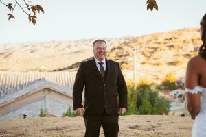 Groom stands on hillside with desert mountains in background during outdoor ceremony.