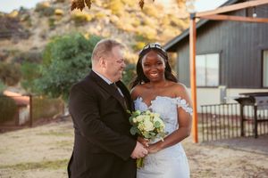 A joyful wedding couple shares a candid moment together outdoors near a rustic venue.