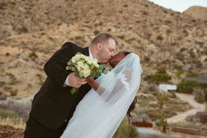 Intimate wedding moment captured against scenic desert hillside backdrop.