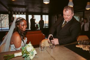 Wedding couple shares drinks at rustic bar setting during reception.