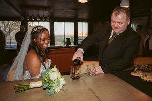 Newlyweds share drinks at a rustic bar during their wedding celebration.