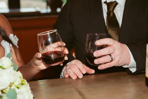 Close-up of wine glasses and hands during wedding toast at wooden table.