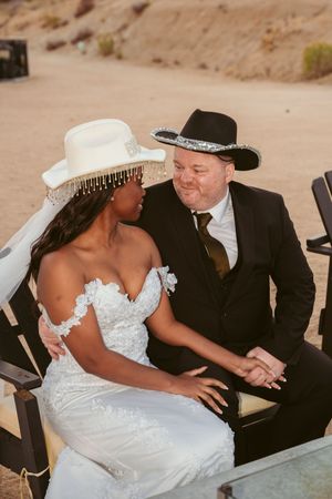 A couple shares an intimate moment at their desert wedding ceremony, with the bride in white and groom in black attire.