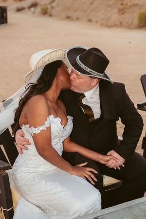 A romantic moment between newlyweds sharing a kiss while wearing matching western-style hats.