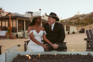 A couple shares an intimate moment together next to a fire pit at an outdoor desert venue during sunset.