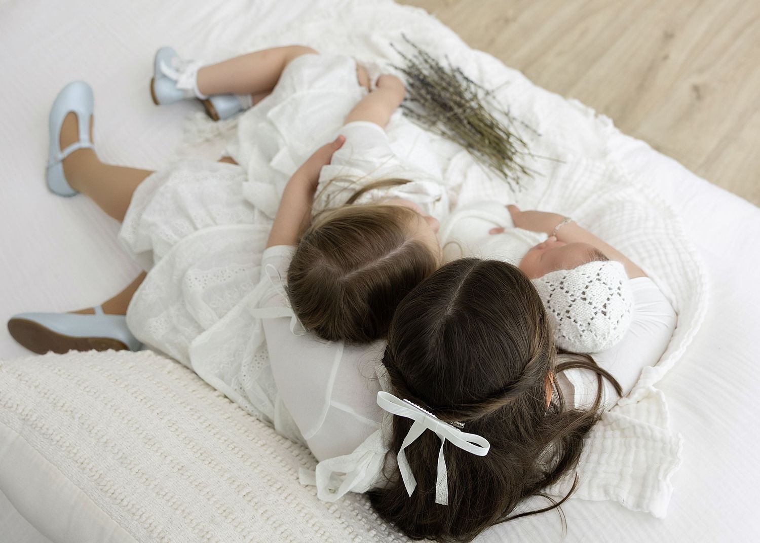 Two young ones sit together in a blooming lavender field at sunset wearing white dresses and straw hats.