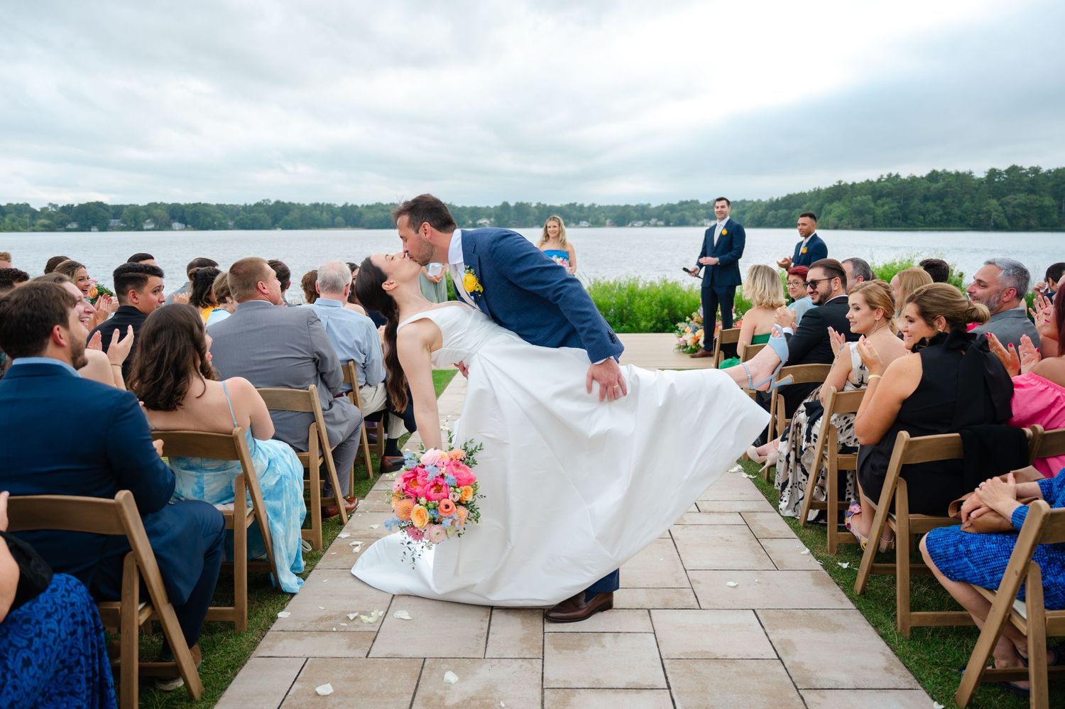 Newlyweds share a dip kiss during their wedding ceremony in Westchester, NY next to a lake.