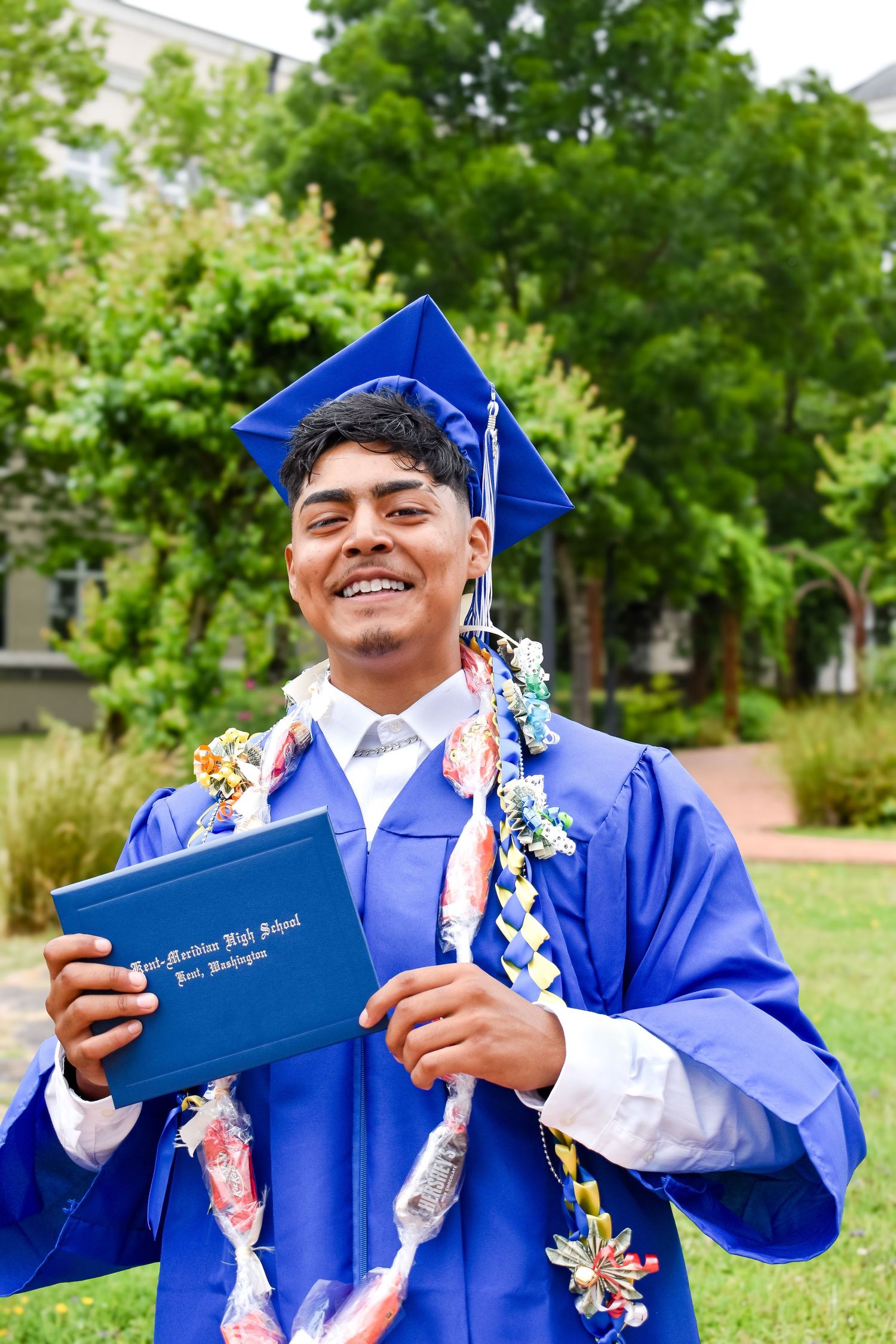 senior portrait at Kent-Meridian High School in Kent, WA celebrating graduation with a blue cap and gown, candy leis, and a proud smile.