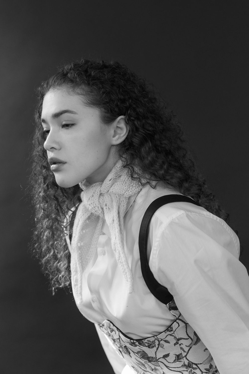 A black and white portrait of a person with natural curly hair wearing a Victorian-style blouse and floral corset.