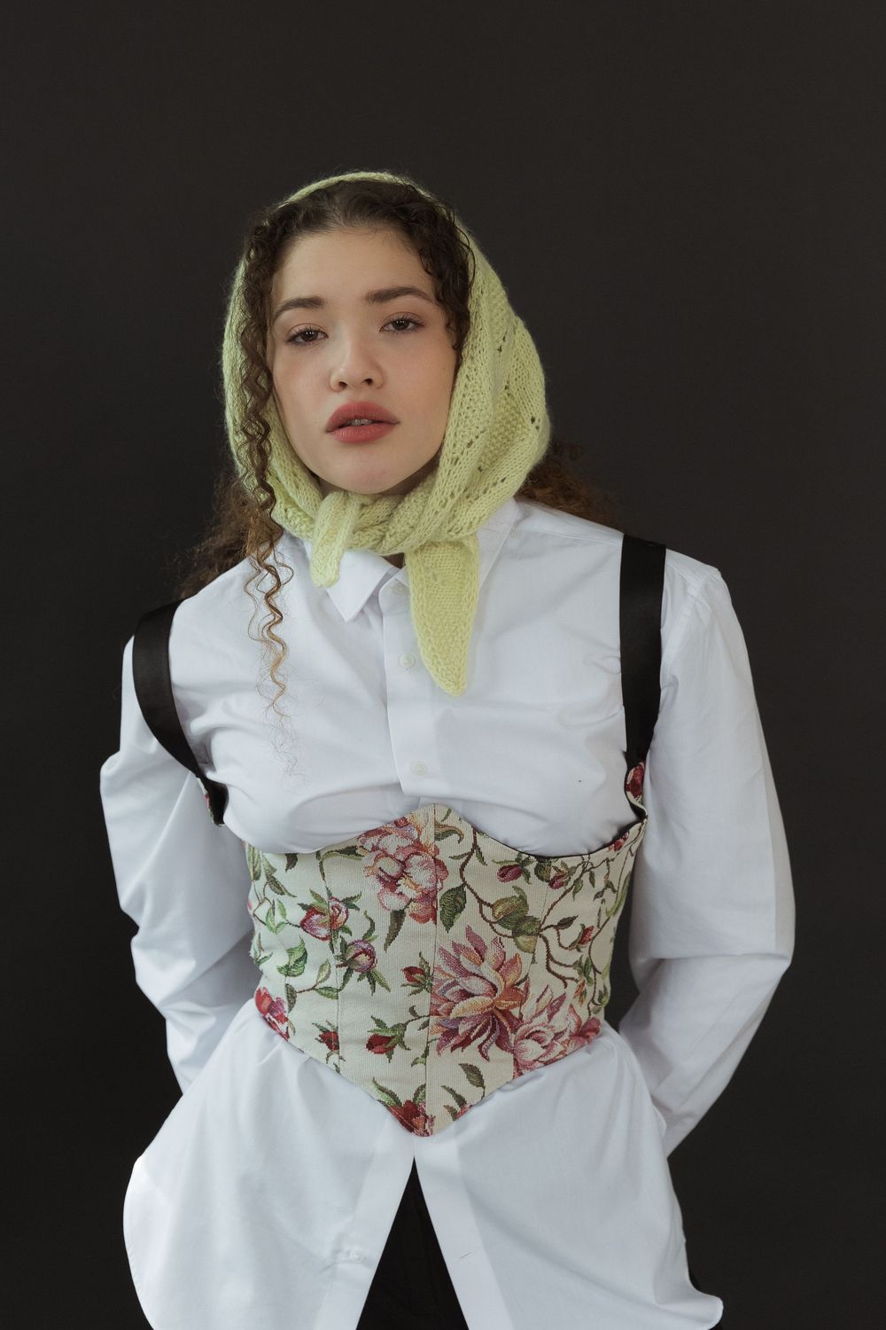 Model wearing white button-down shirt with floral corset and lime green headscarf against dark background.