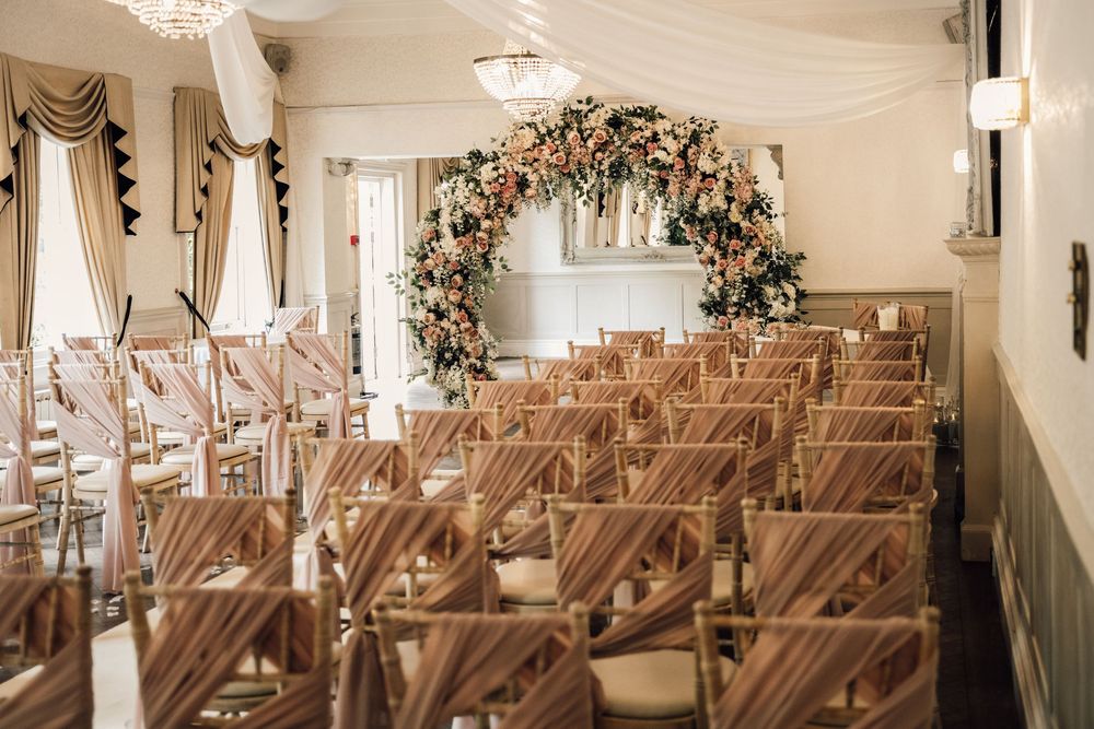 Wedding ceremony venue with wooden chairs and floral arch under crystal chandeliers.