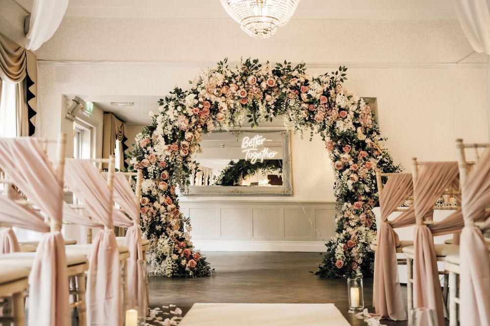 Indoor wedding venue with romantic floral arch and elegant chandelier lighting.