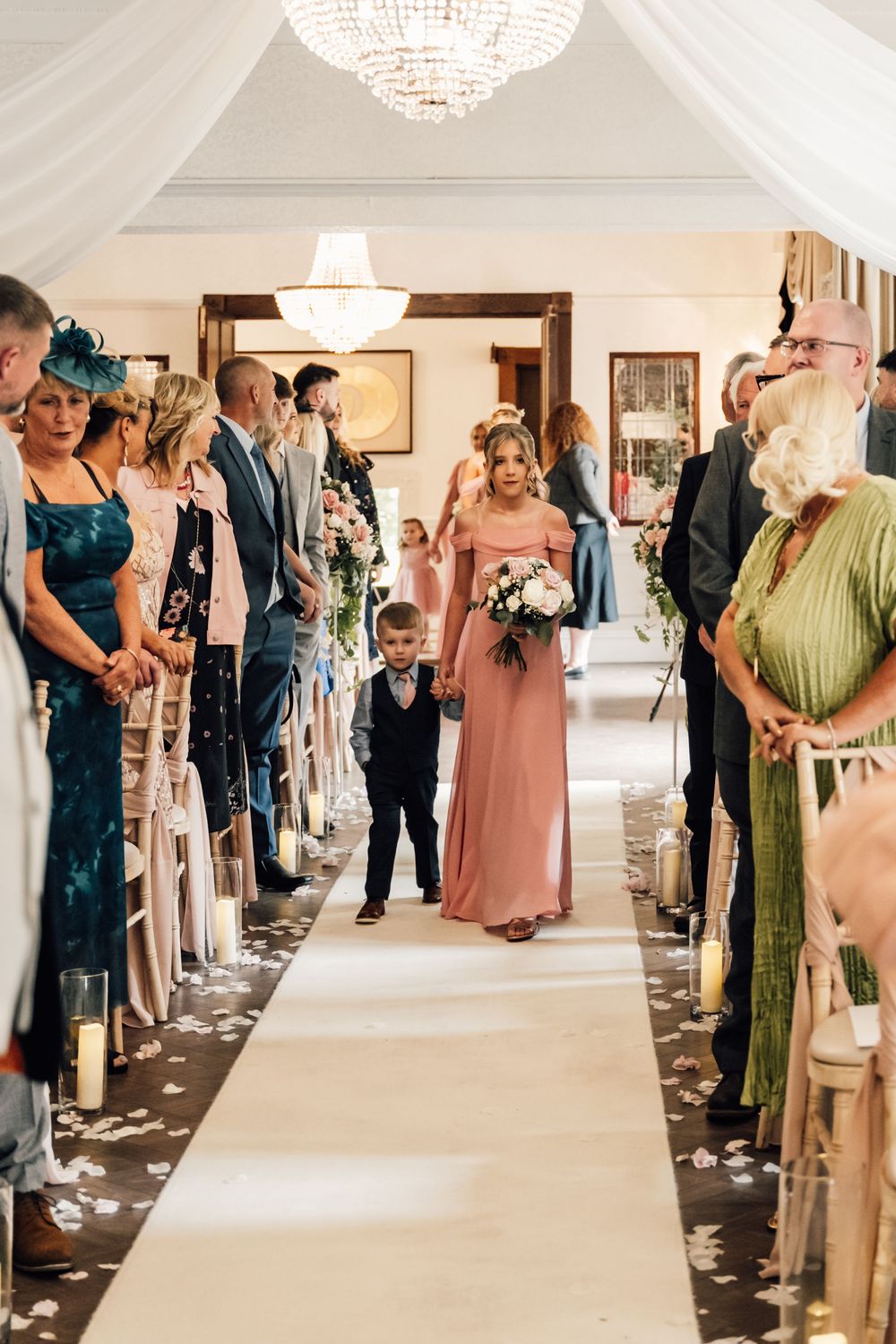 Wedding ceremony processional in an elegant white room with guests lining the aisle.