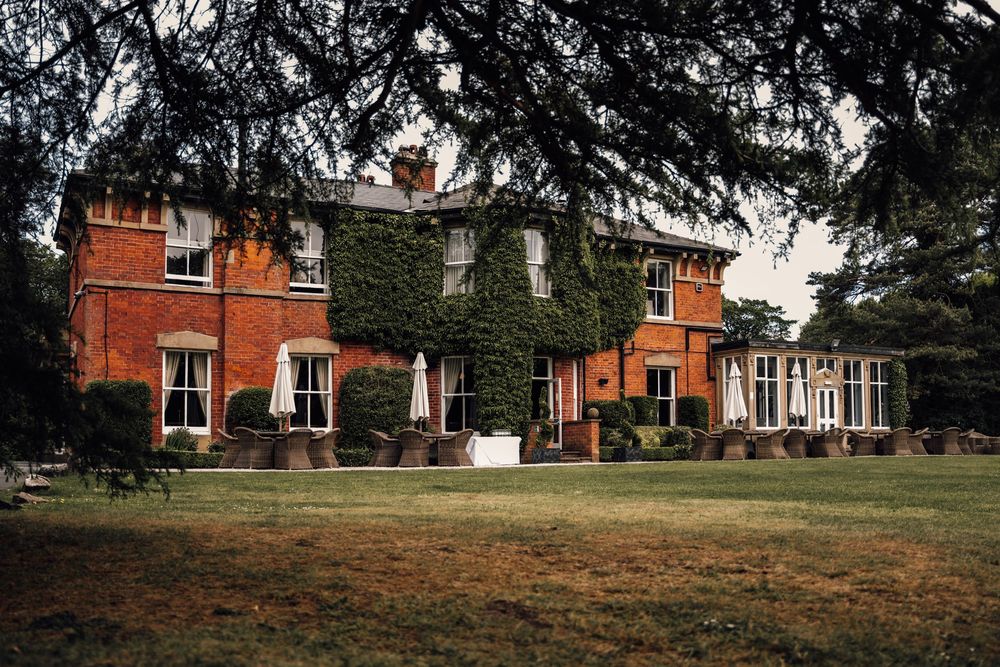 Panoramic view of a historic red brick mansion with sprawling lawn and mature trees.