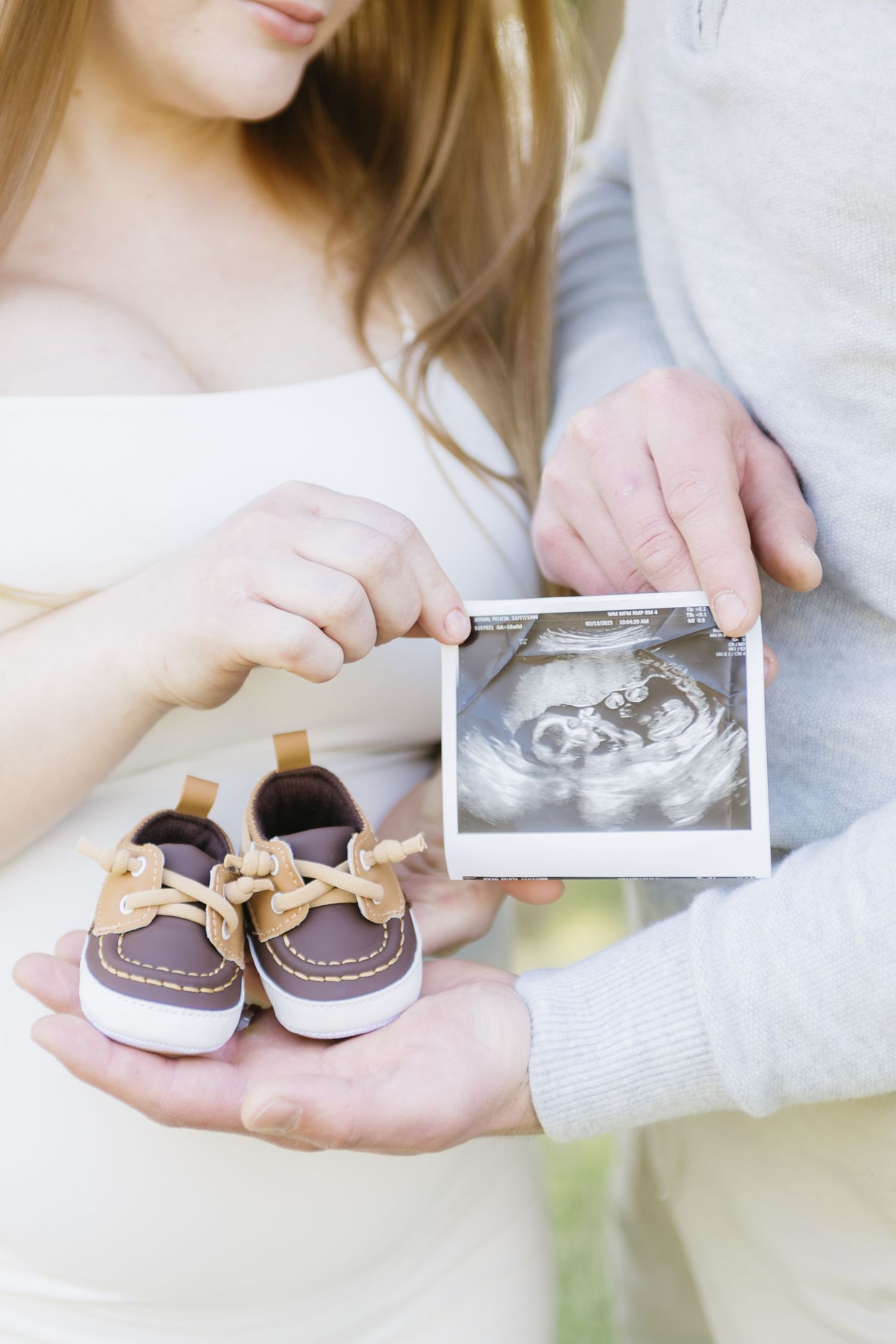 Couple holding baby shoes and ultrasound photo in tender pregnancy announcement.