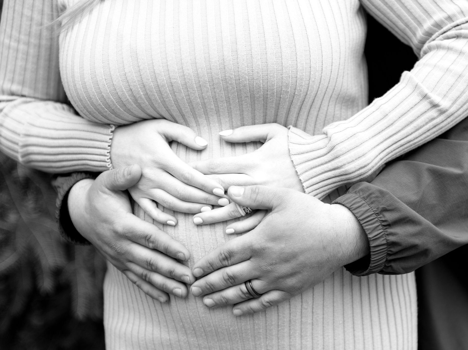 Black and white close-up of hands tenderly cradling a pregnant belly.