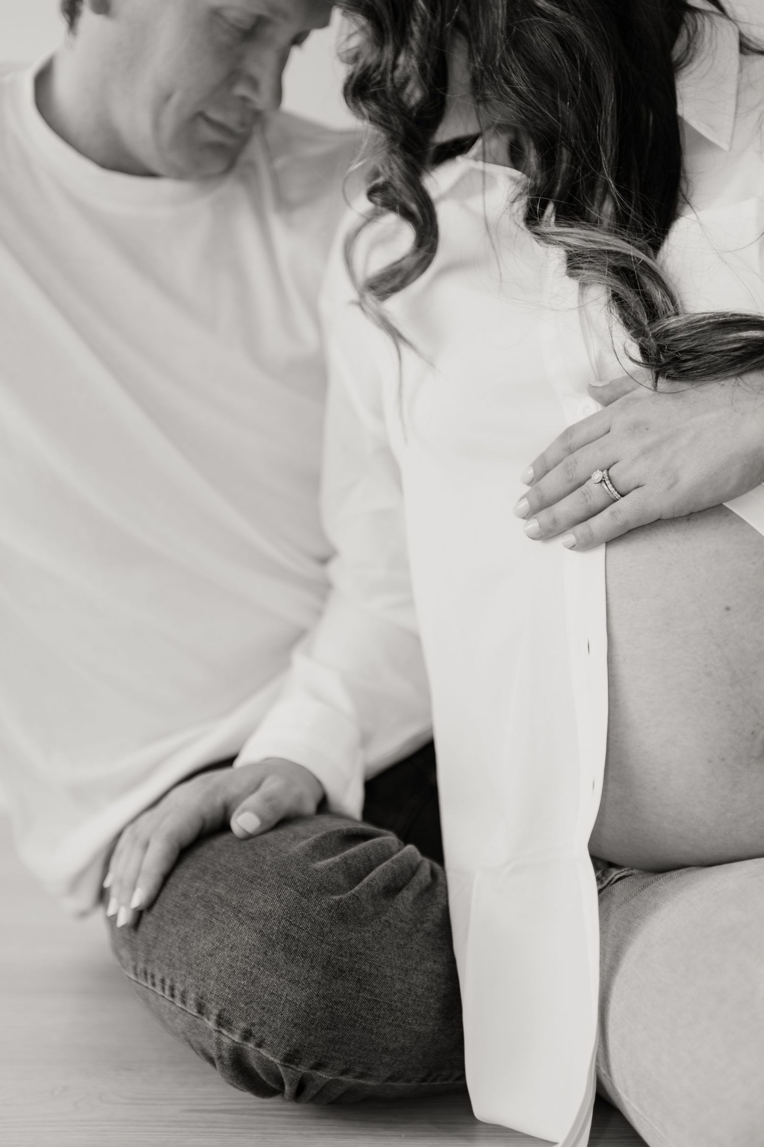 Black and white intimate maternity moment with couple in white clothing.
