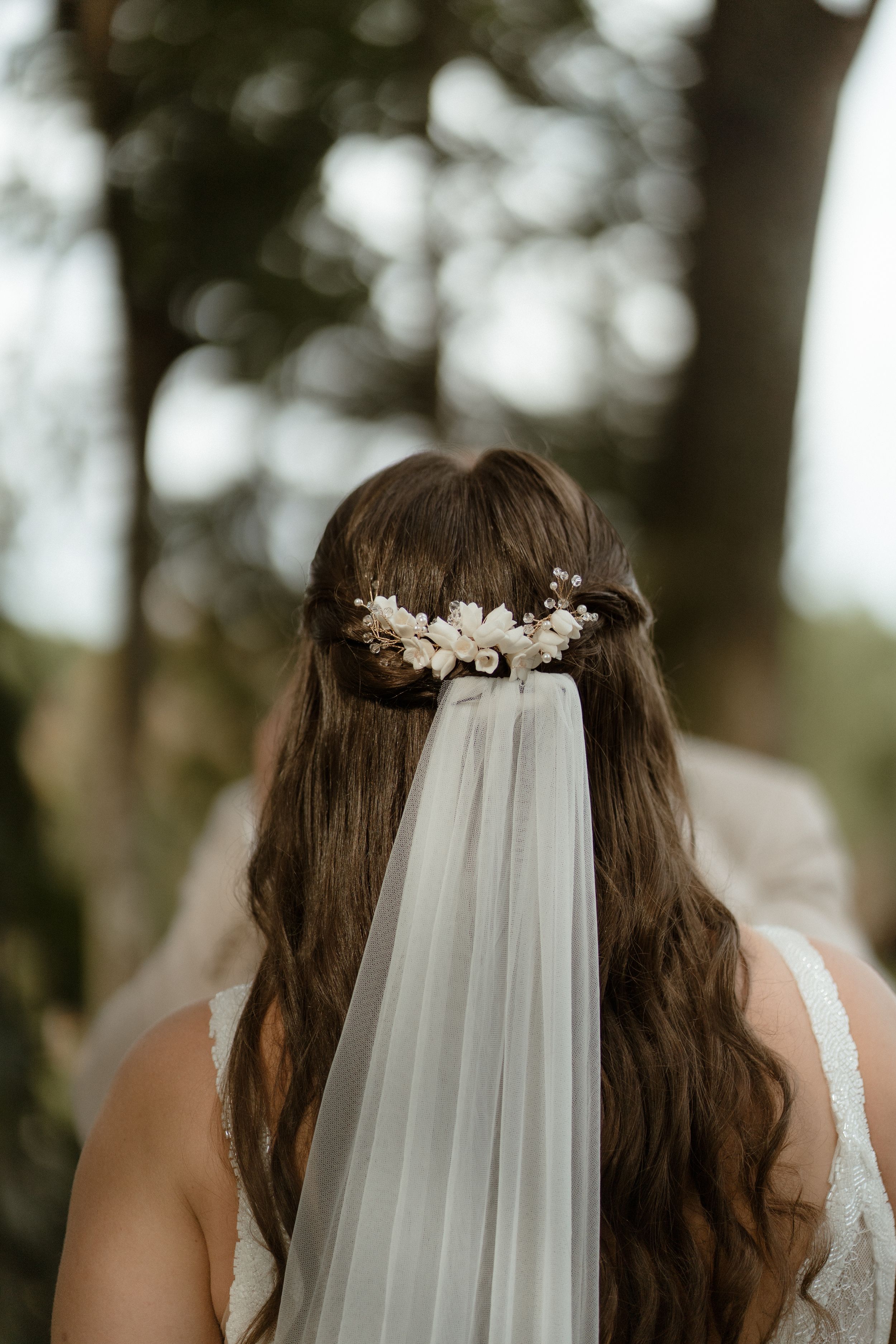 Close-up view of a white wedding veil adorned with delicate floral hairpieces against a natural outdoor backdrop.