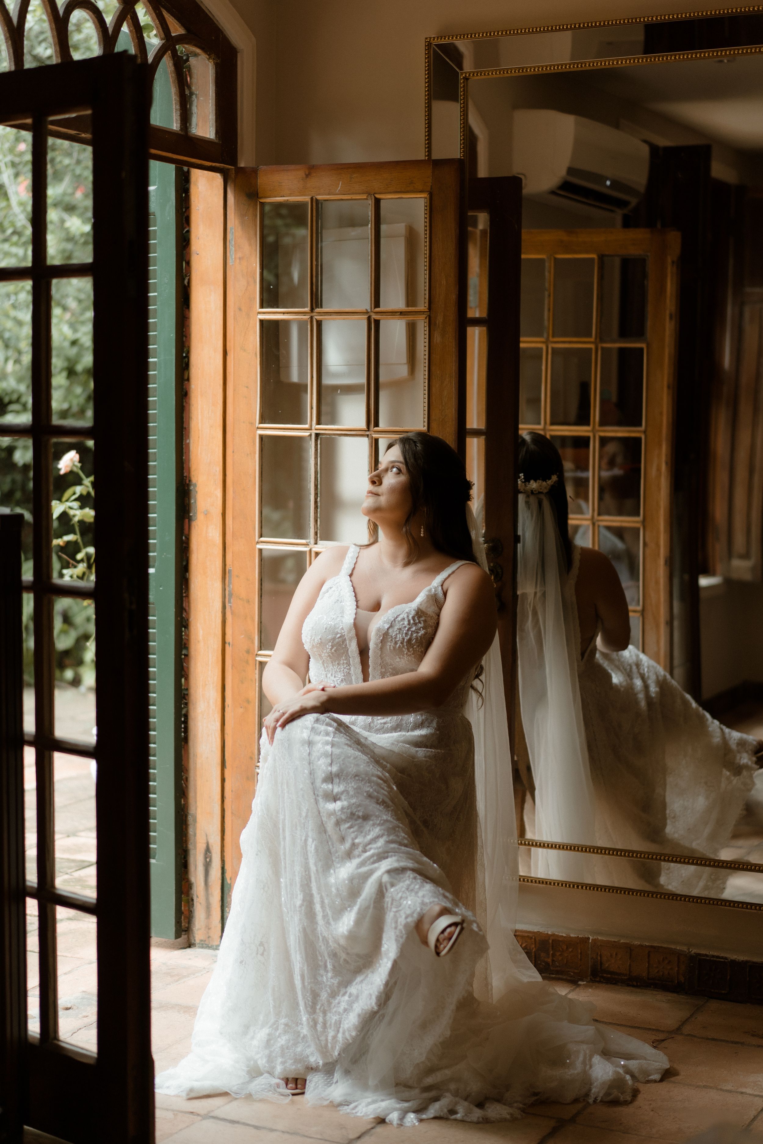 Elegant bridal portrait in a white lace gown by a windowed doorway.