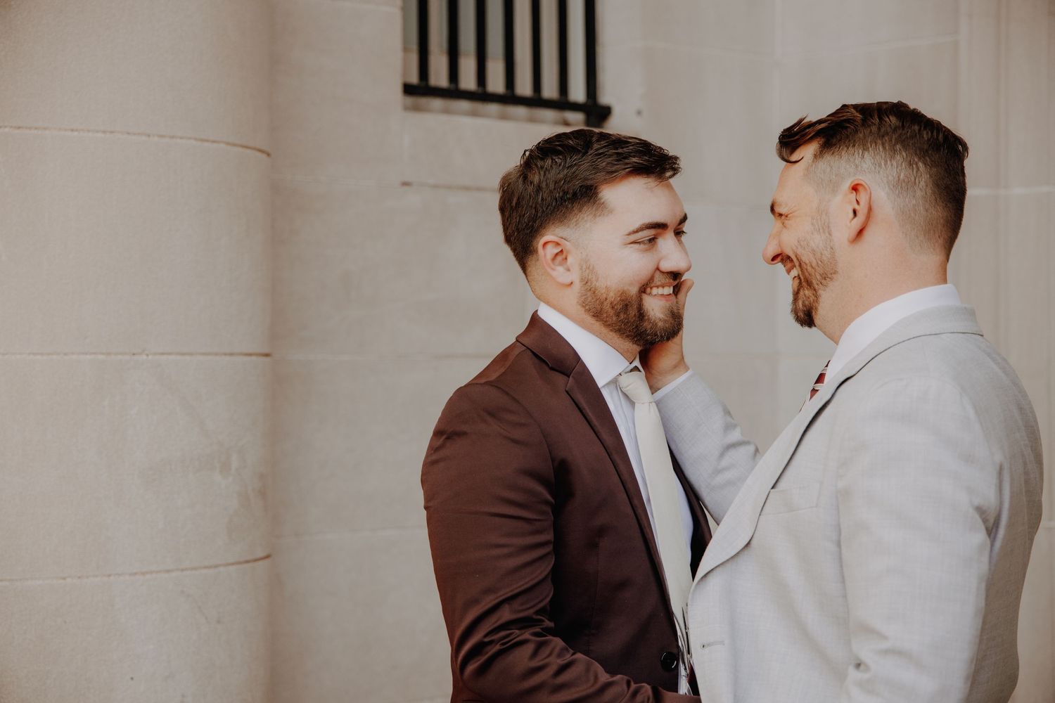 Two people in contrasting suits share a tender moment against a light background.