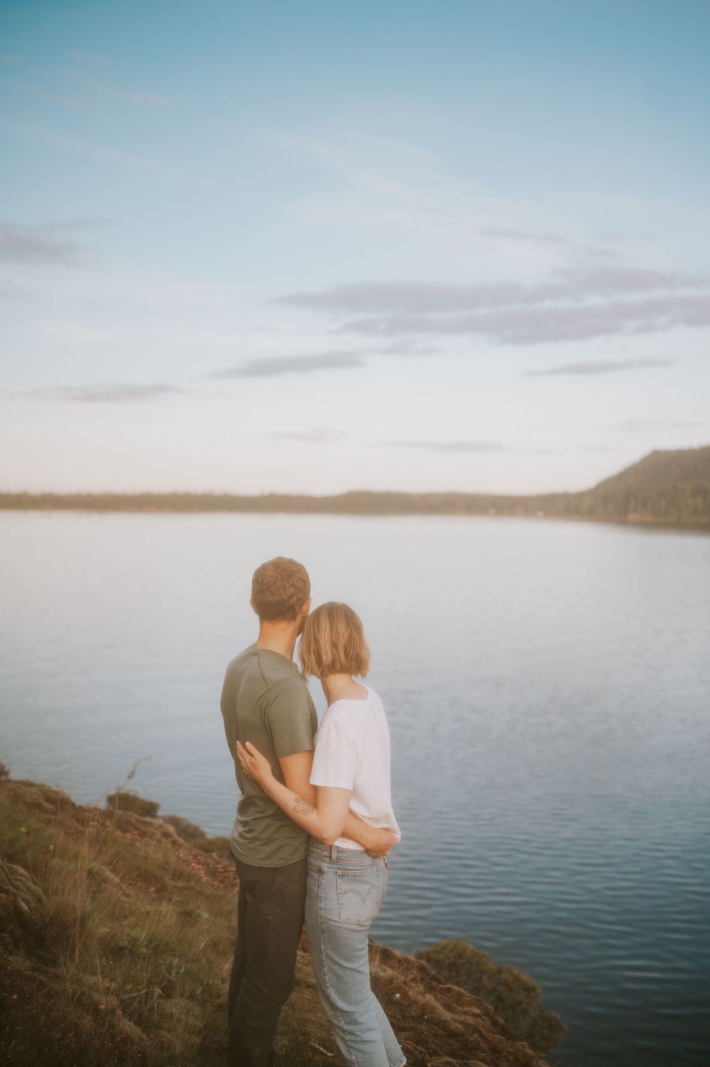 Engaged couple standing on rocky cliff overlooking Comox Lake, holding hands during sunset for the engagement photoshoot