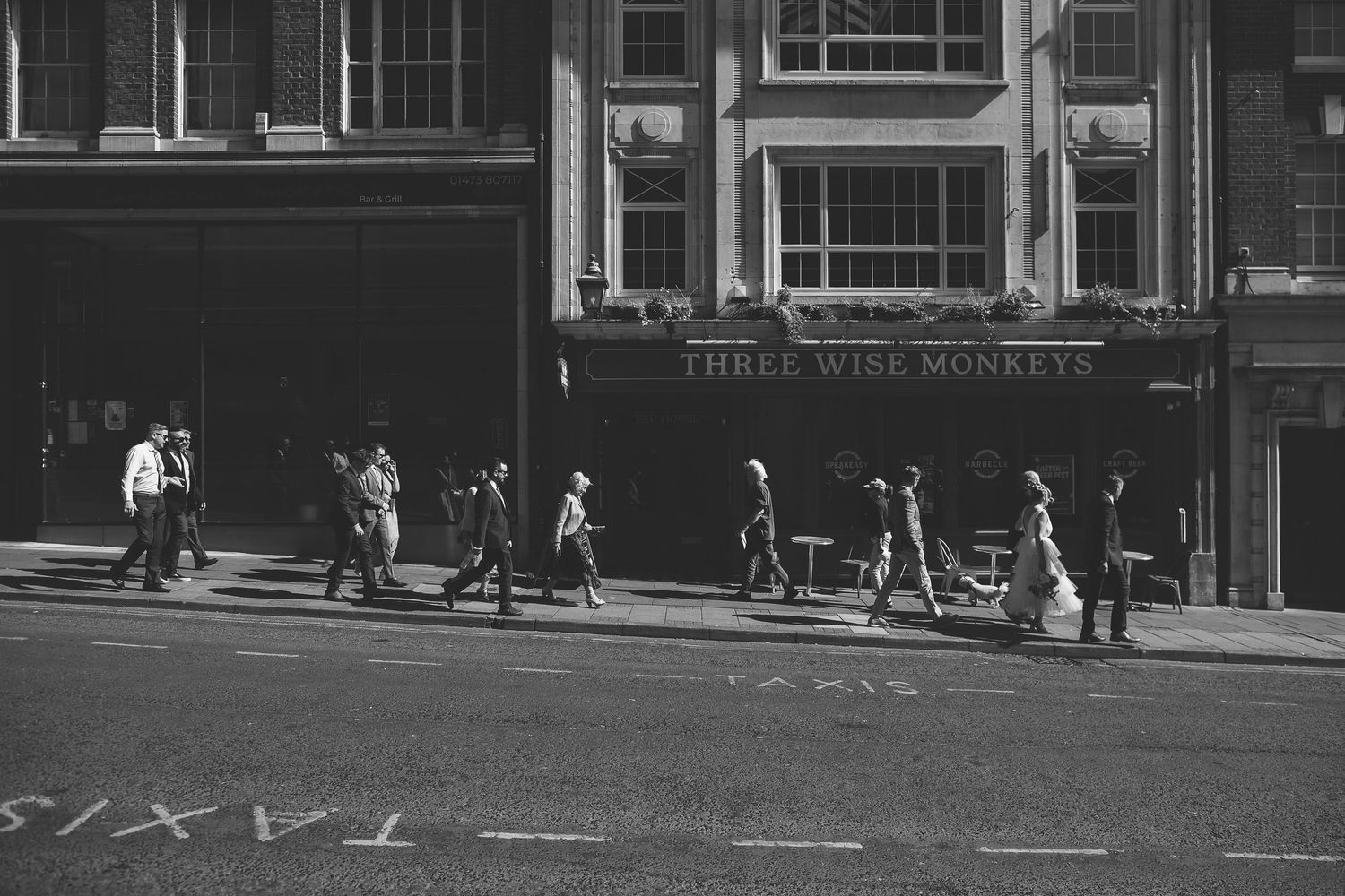 People walking on a busy urban street in front of storefronts in black and white photography.